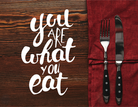 top view of fork and knife on dark red tablecloth on wooden background with you are what you eat...