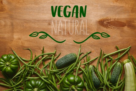 Green beans and organic vegetables on wooden table with "vegan natural" letteringの写真素材