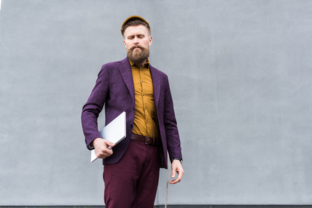 Stylish bearded businessman standing with laptopの写真素材