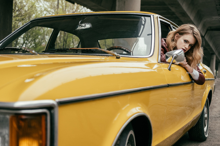 attractive young woman looking at camera while sitting in yellow vintage car