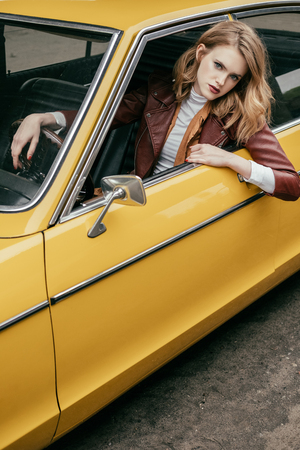 beautiful stylish girl looking at camera through window of yellow retro carの写真素材