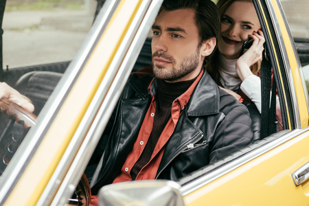 handsome young man driving car while smiling girlfriend sitting behind