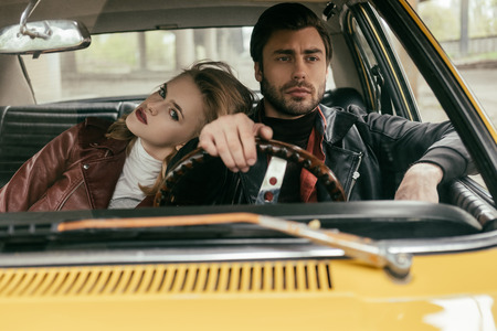 beautiful stylish young couple in leather jackets sitting together in classic car