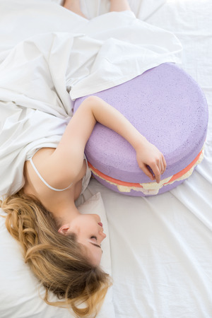 top view of beautiful girl sleeping with big purple macaron on bedの写真素材