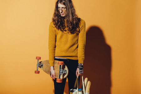handsome skater holding longboard and bag with food, on yellowの写真素材