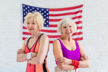 beautiful sporty senior women standing with crossed arms and smiling at camera against american flagの写真素材