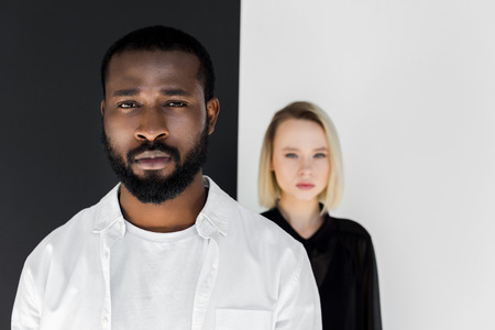 multicultural couple looking at camera near black and white wall, yin yang conceptの写真素材