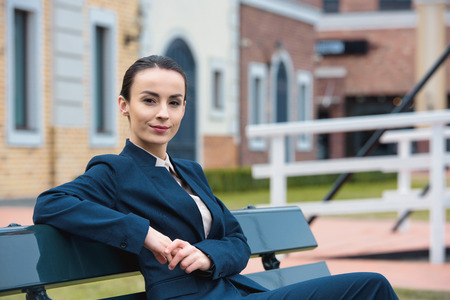 beautiful businesswoman sitting on bench and looking at cameraの写真素材