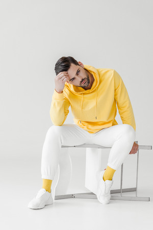 stylish young man in yellow hoodie sitting on flipped chair on whiteの写真素材