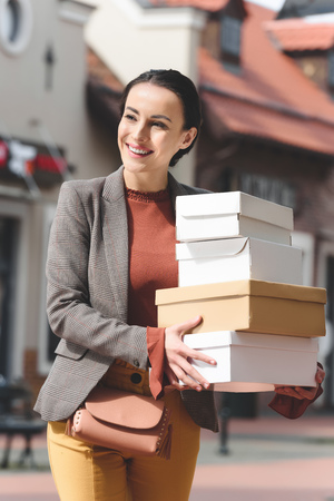 smiling attractive woman holding shopping boxes and looking awayの写真素材