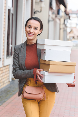 smiling attractive woman holding shopping boxes and looking at cameraの写真素材