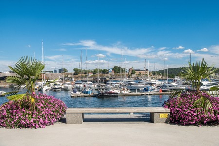 OSLO, NORWAY - 28 JULY, 2018: cozy empty bench, beautiful flowering plants and moored boats in harbourのeditorial素材