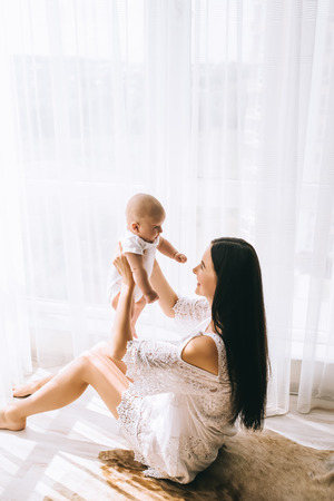 smiling young mother playing with her baby while sitting on floor at homeの写真素材