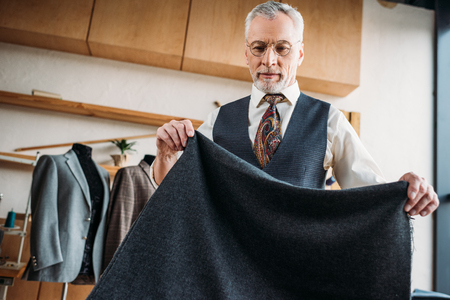 handsome mature tailor with grey cloth at sewing workshopの写真素材
