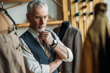 handsome mature man looking at jackets on hangers in storeの写真素材