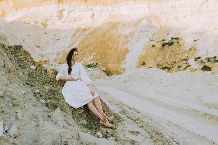 elegant girl in white dress and straw hat sitting in sandy canyonの写真素材