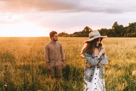young stylish couple walking on meadow at sunsetの写真素材