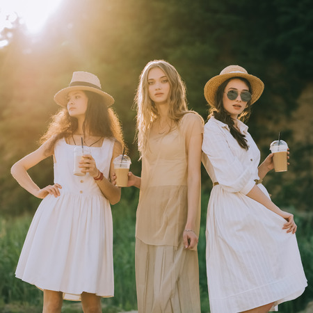 attractive stylish girls in straw hats holding coffee latte posing, with sunlightの写真素材