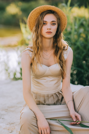 beautiful girl in straw hat sitting on ground near lakeの写真素材