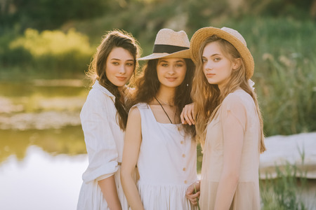 elegant pretty young women in straw hats standing near lakeの写真素材