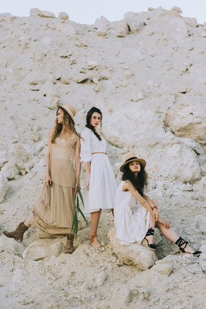 stylish elegant girls in trendy dresses and straw hats posing together in sandy canyonの写真素材