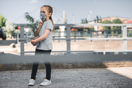 child in protective mask carrying green potted plant, air pollution conceptの素材 [FY310109551470]