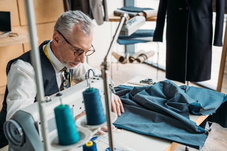 handsome tailor sewing blue cloth with sewing machine at sewing workshopの写真素材