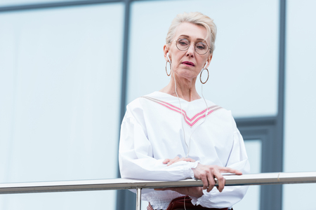 stylish senior woman in trendy outfit listening music with earphonesの写真素材