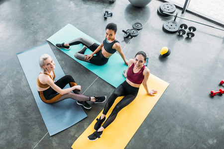 high angle view of young multicultural sportswomen resting on mats after training at gymの写真素材