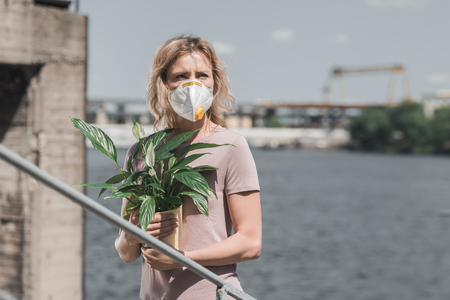 woman in protective mask holding potted plant on bridge, air pollution conceptの写真素材