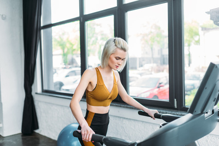 side view of young sportswoman running on treadmill at gym