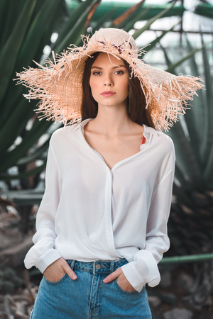 attractive young woman in summer outfit and straw hat posing in tropical gardenの写真素材