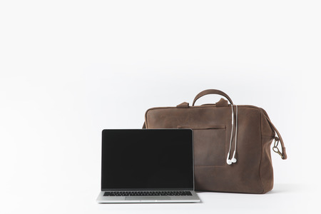 close up view of laptop with blank screen and stylish bag with earphones isolated on whiteの写真素材