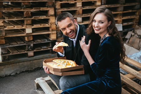 side view of happy stylish couple with italian cheese pizza resting on streetの写真素材