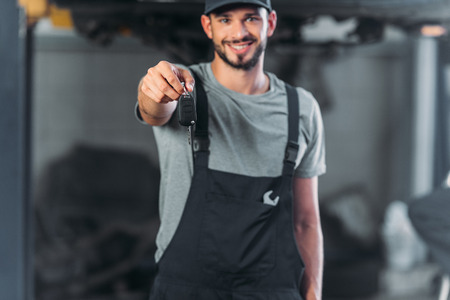 smiling mechanic holding car key in auto repair shopの写真素材