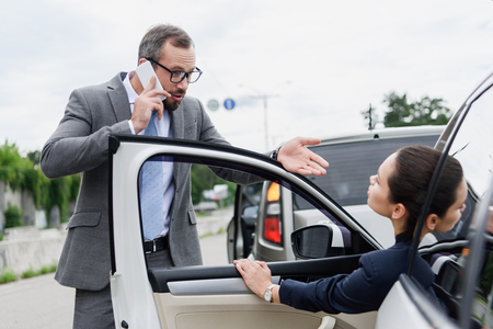 businesspeople quarreling on road after car accident, man talking by smartphoneの写真素材