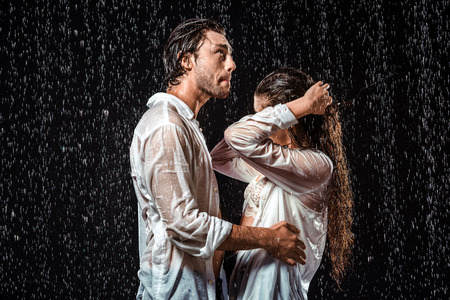 side view of couple in white shirts standing under rain isolated on black