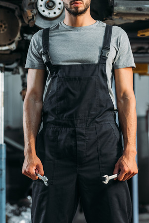 cropped view of professional auto mechanic holding two wrenches in workshopの写真素材