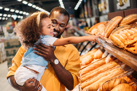 african american little child pointing by finger at pastry to father in supermarketの写真素材