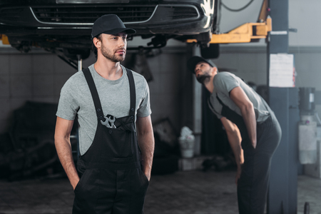 auto mechanic in overalls with colleague working in workshop behindの写真素材