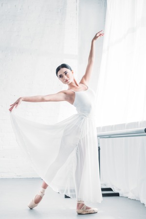 elegant young ballerina in white dress dancing in ballet studioの写真素材