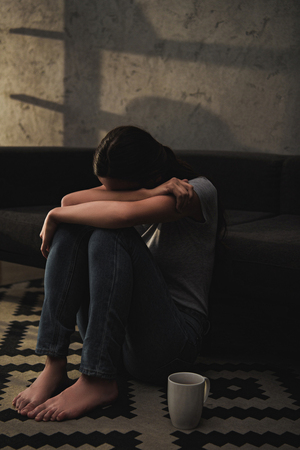 emotional crying woman hugging her knees while sitting on floor at sofaの写真素材