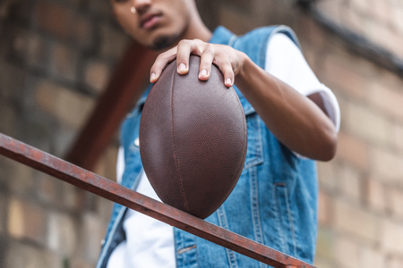 selective focus of american football ball in hand of young man at streetの写真素材