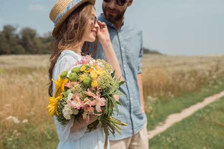 side view of smiling woman with bouquet of wild flowers and boyfriend near by in fieldの写真素材