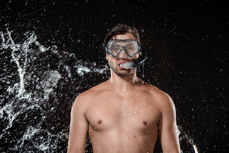 portrait of shirtless man in swimming mask with snorkel swilled with water isolated on blackの写真素材