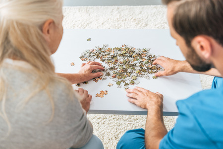 cropped shot of senior woman and young caregiver playing with jigsaw puzzle piecesの写真素材