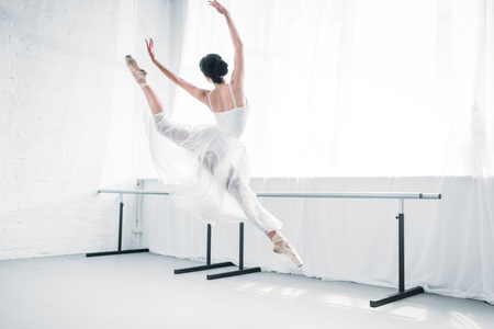 back view of graceful young ballerina in white dress dancing in ballet studioの写真素材