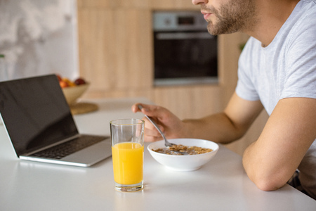 cropped image of man eating flakes at kitchen table with fresh juice and laptopの写真素材