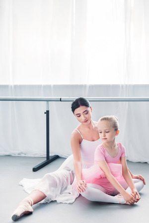 beautiful young ballerina looking at child in pink tutu exercising in ballet schoolの写真素材