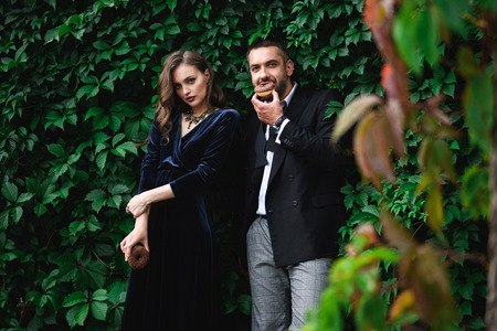 fashionable couple with chocolate doughnuts with green foliage behind looking at camera